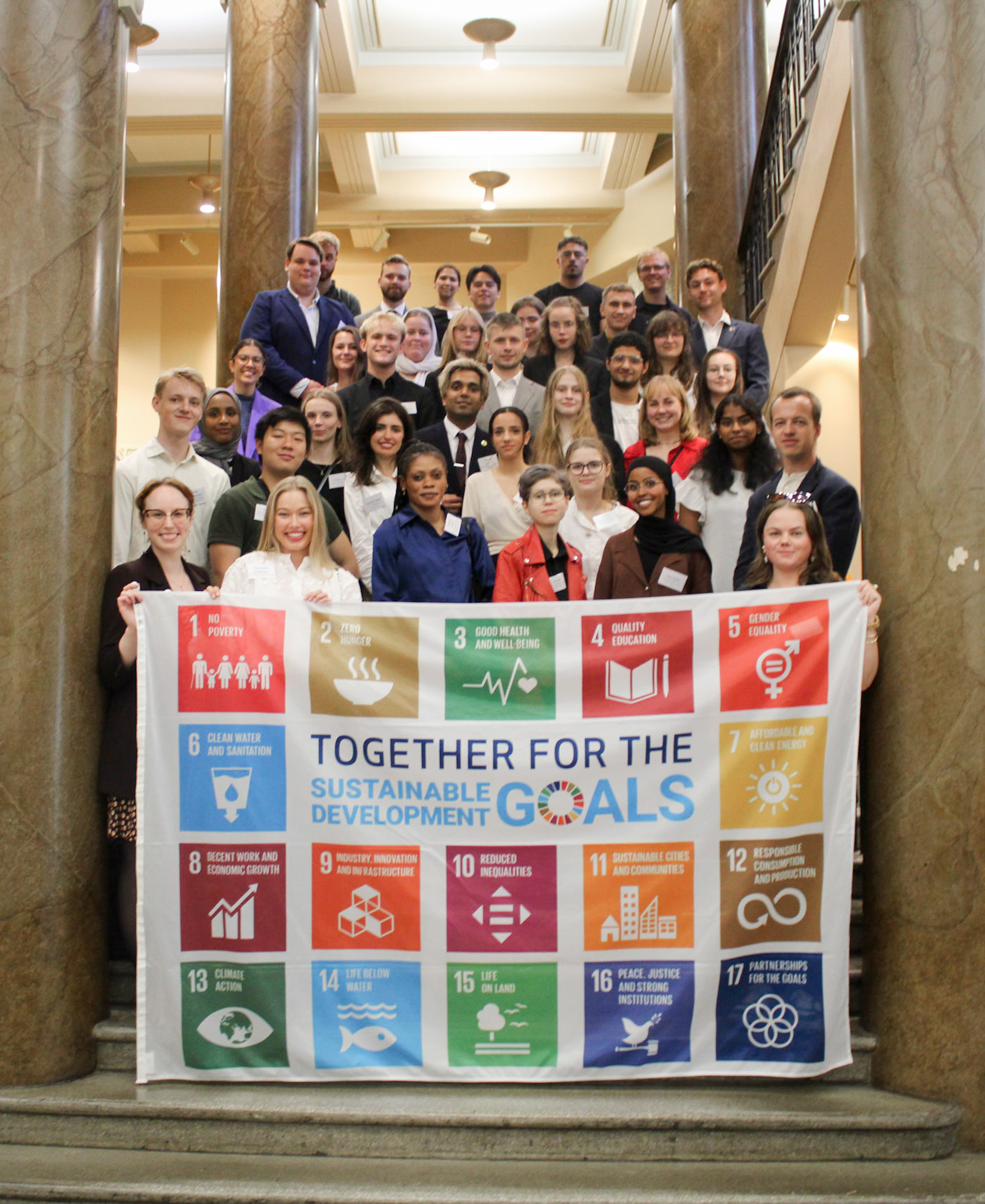 In the picture are about 40 young people standing on stairs with a sustainable development goals flag in the front.